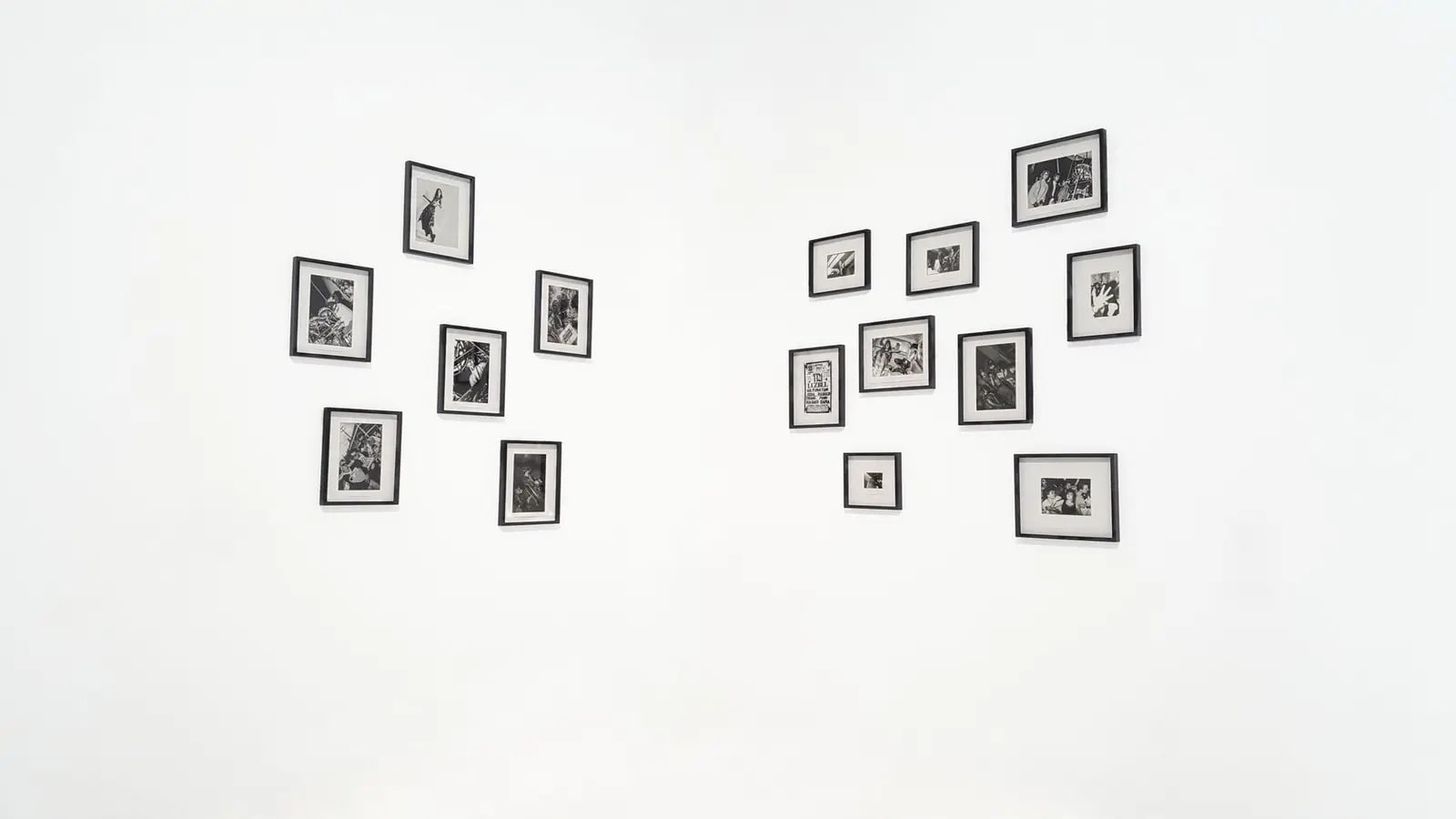 Two clusters of small black-framed photographs hung on a plain white gallery wall