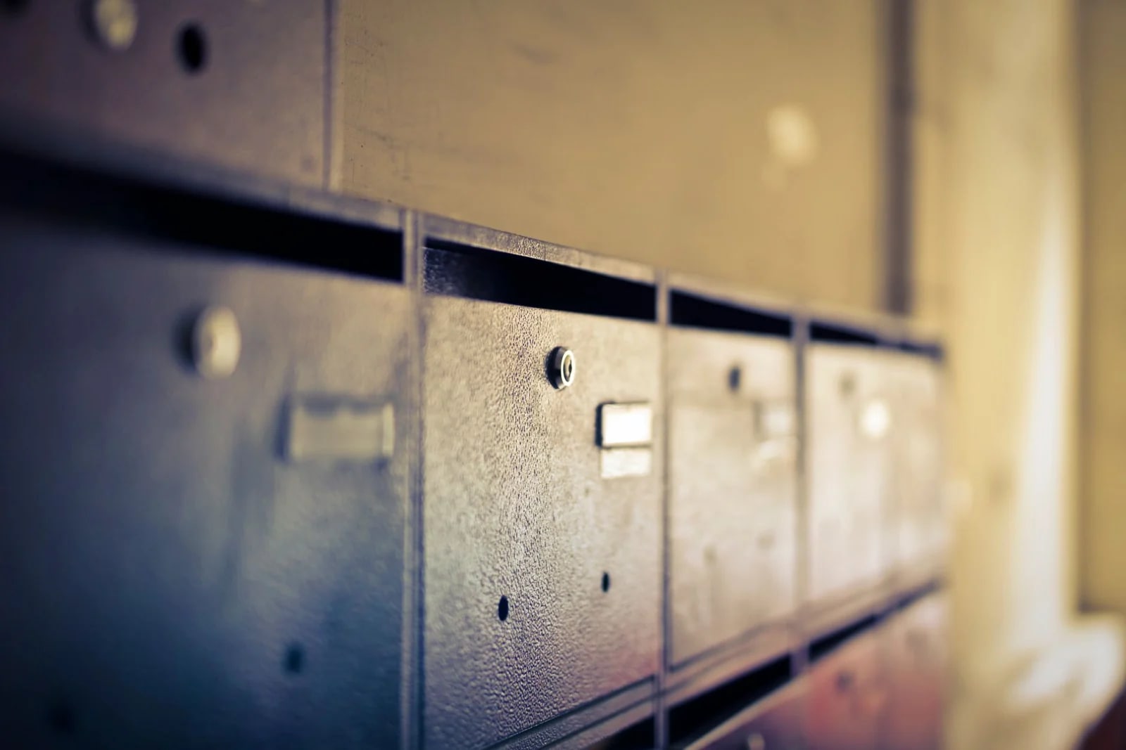 A row of vintage metal mailbox doors with keyholes, receding into soft focus