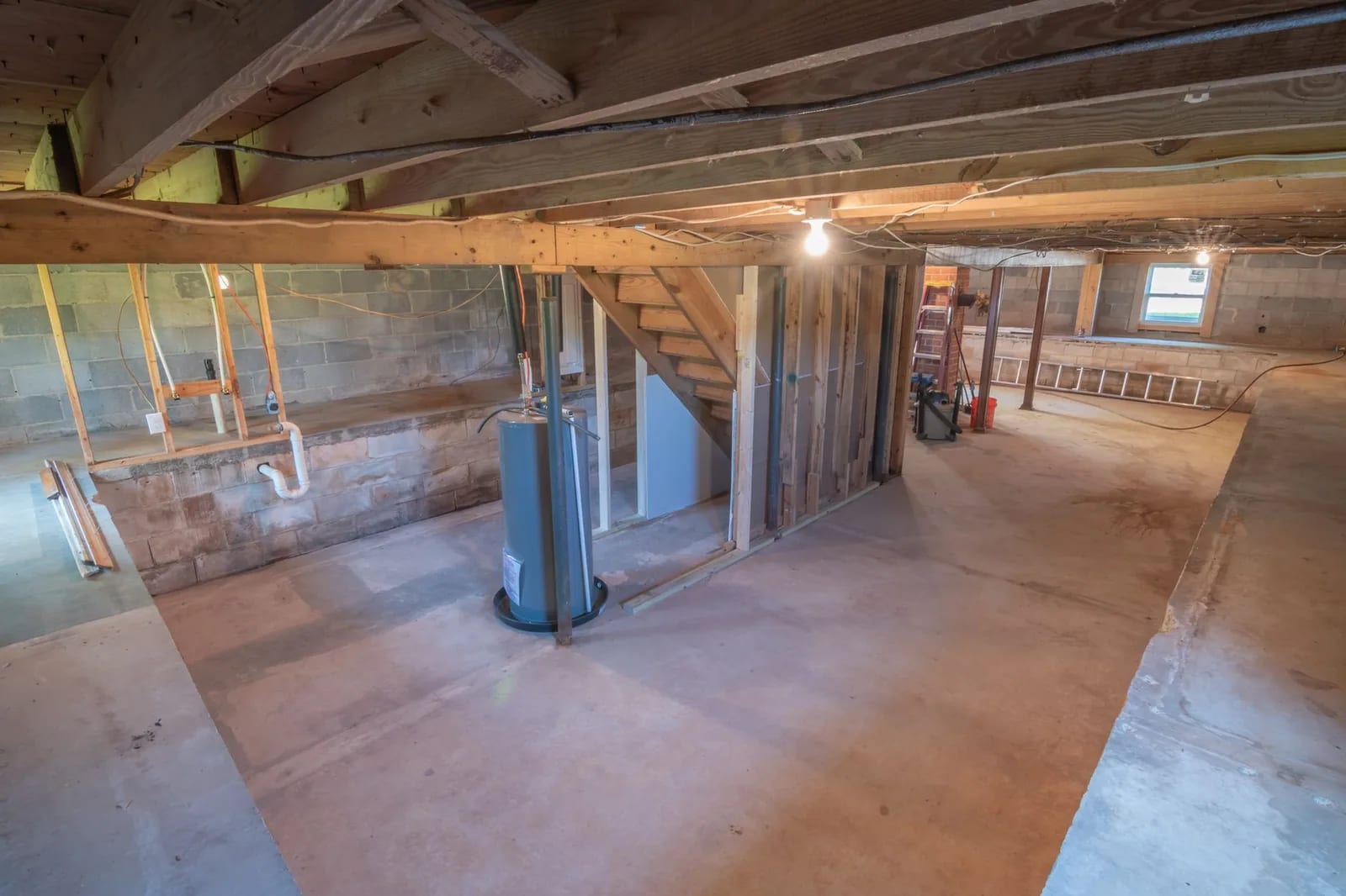 An unfinished basement with a bare concrete floor, concrete block walls, exposed floor joists and a water heater