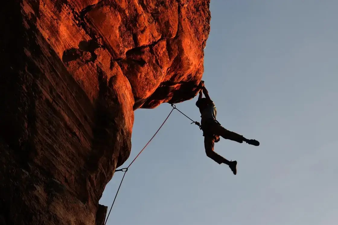 A climber hanging beneath a red sandstone overhang