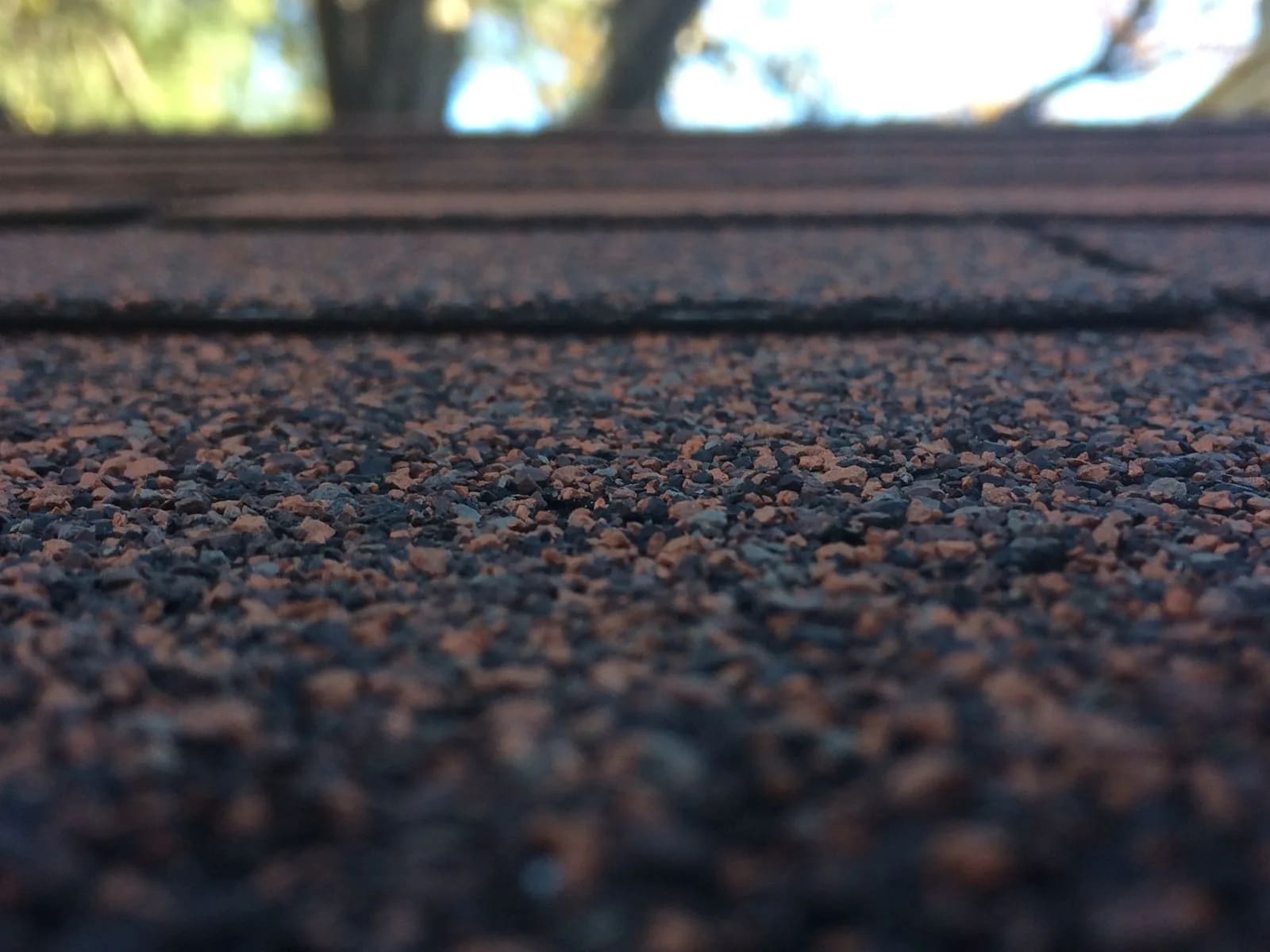 Close-up of the mineral granule surface of asphalt roof shingles, with overlapping courses receding behind