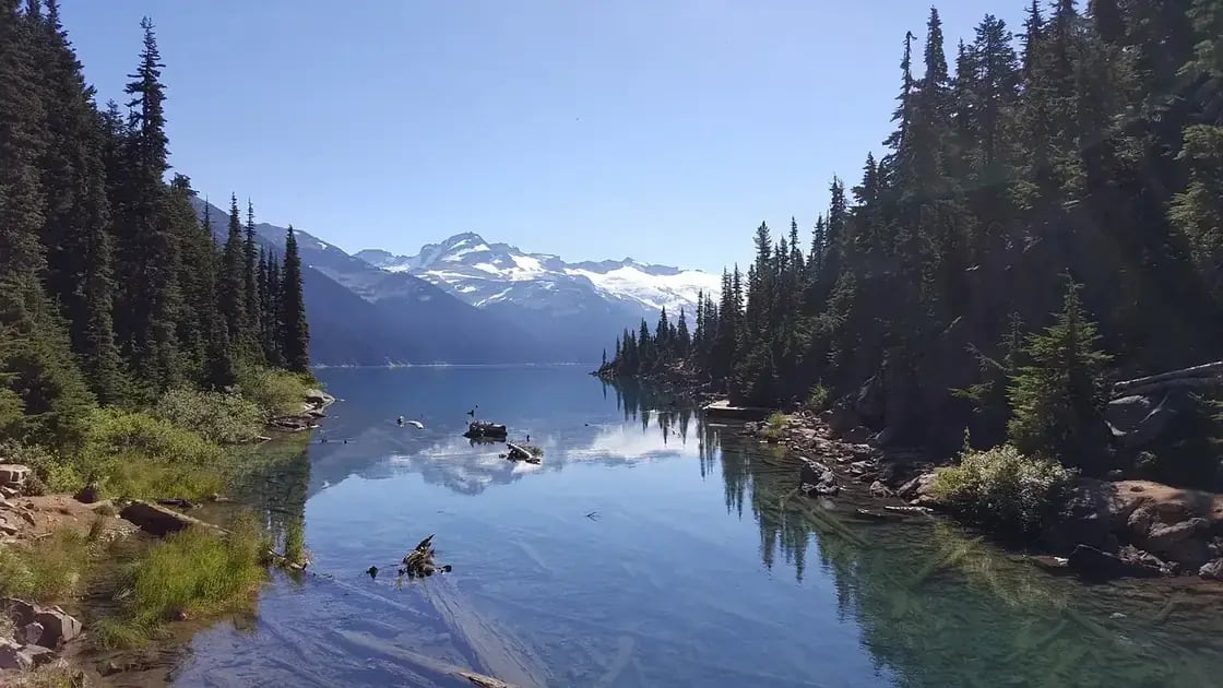 A still lake edged with conifers below a snow-covered peak