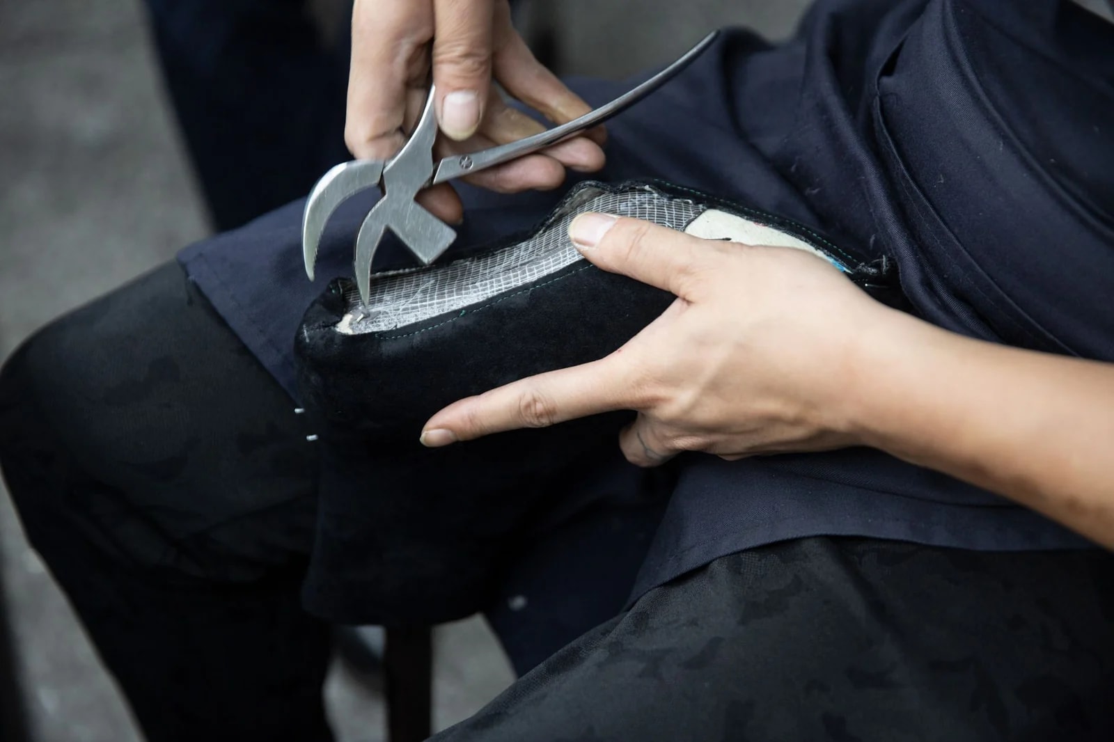 Hands using lasting pincers to pull the upper of a black shoe back over its insole