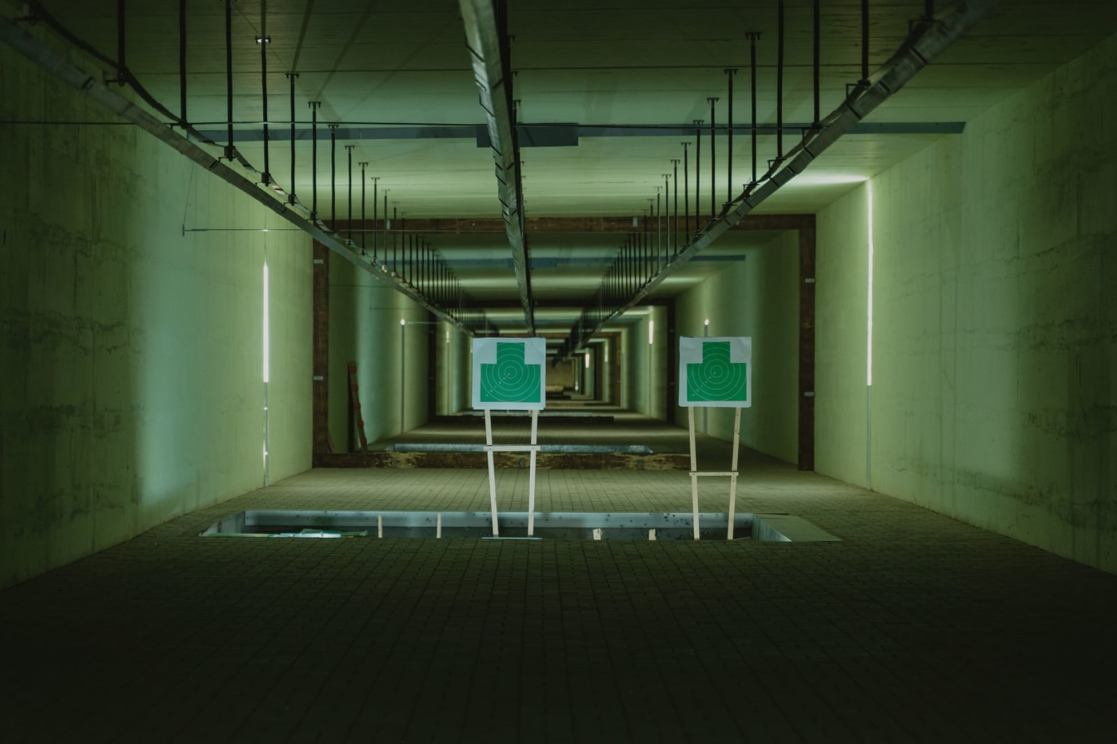 A concrete indoor shooting range corridor lit overhead, with two paper target frames standing downrange