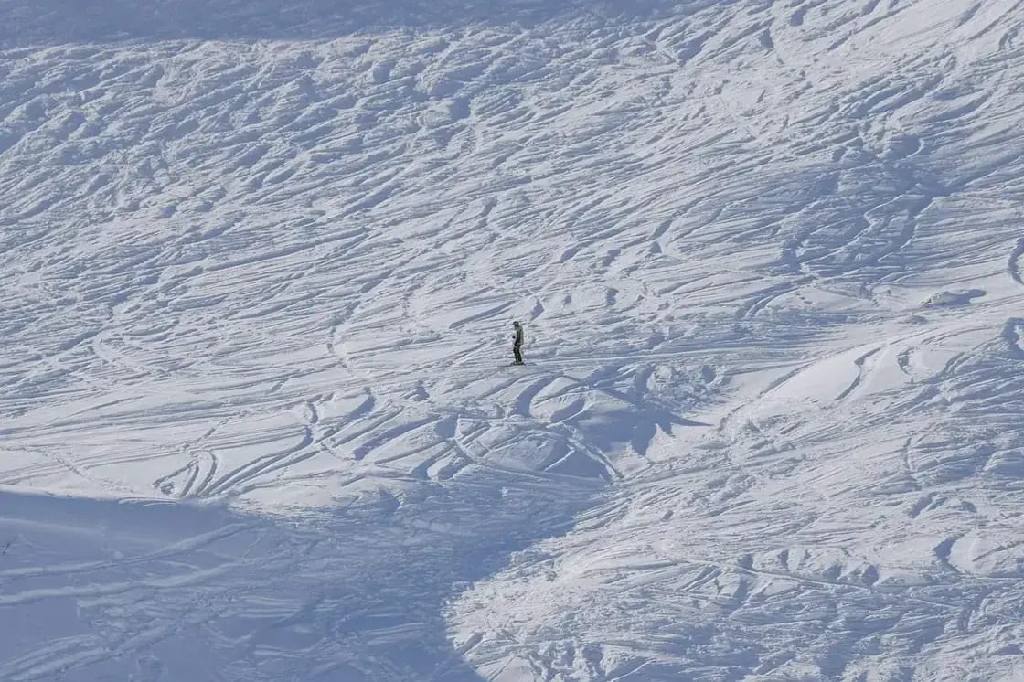 Ski tracks carved across an open snowfield with a lone skier below