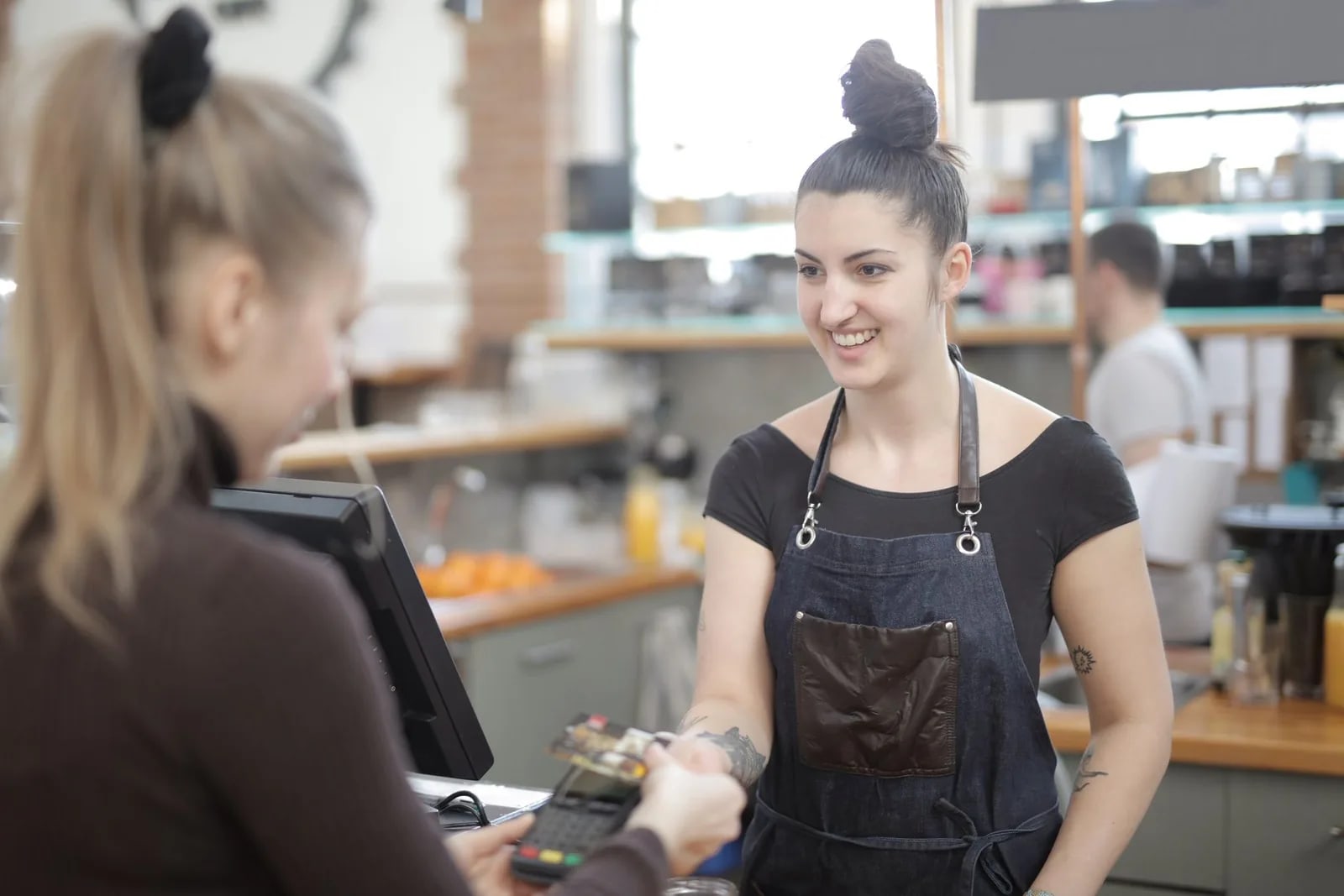 A barista taking a card payment from a customer at a cafe counter