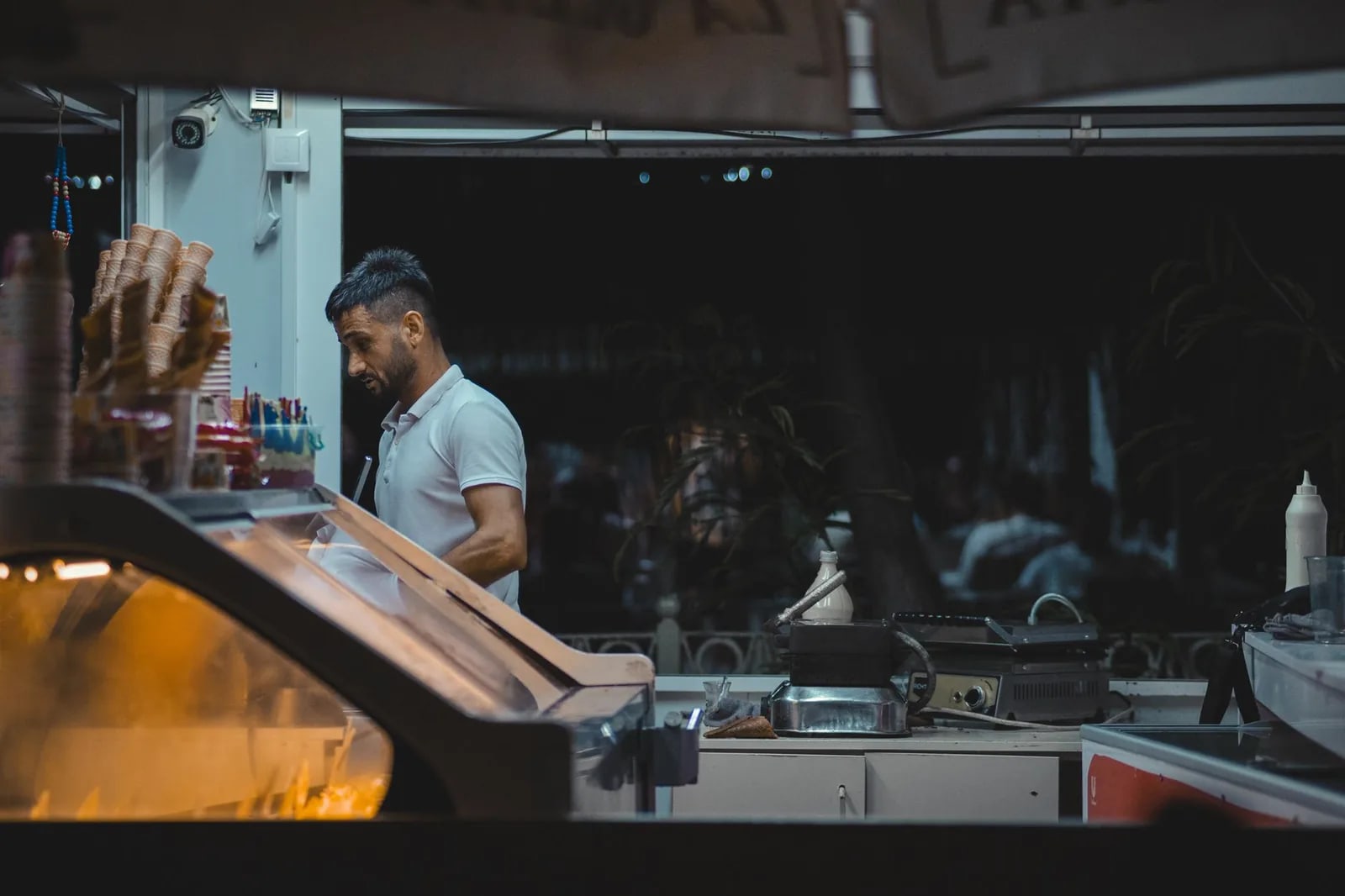 An employee working behind the counter of an ice cream shop in the evening