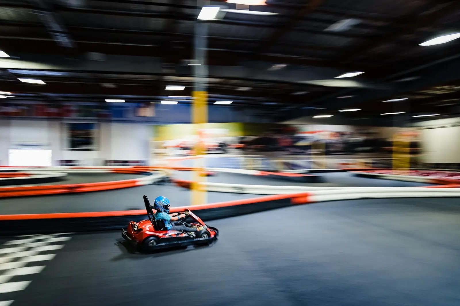 A single go-kart rounding an indoor track lined with red and white barriers, the background blurred by motion
