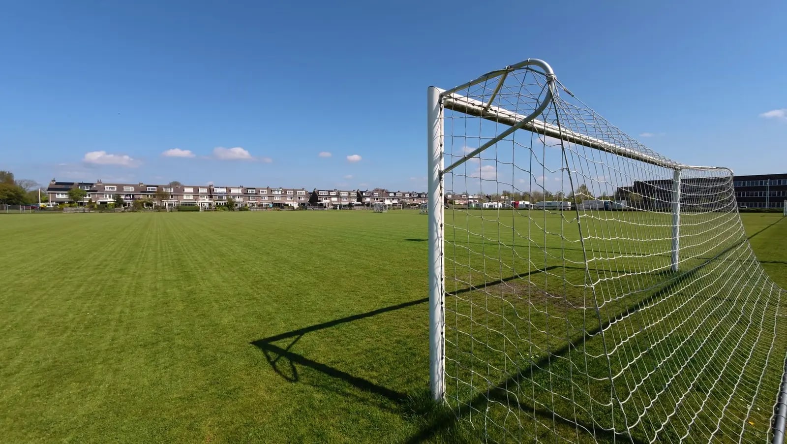A wide view of an empty soccer field with a goal post under a clear blue sky