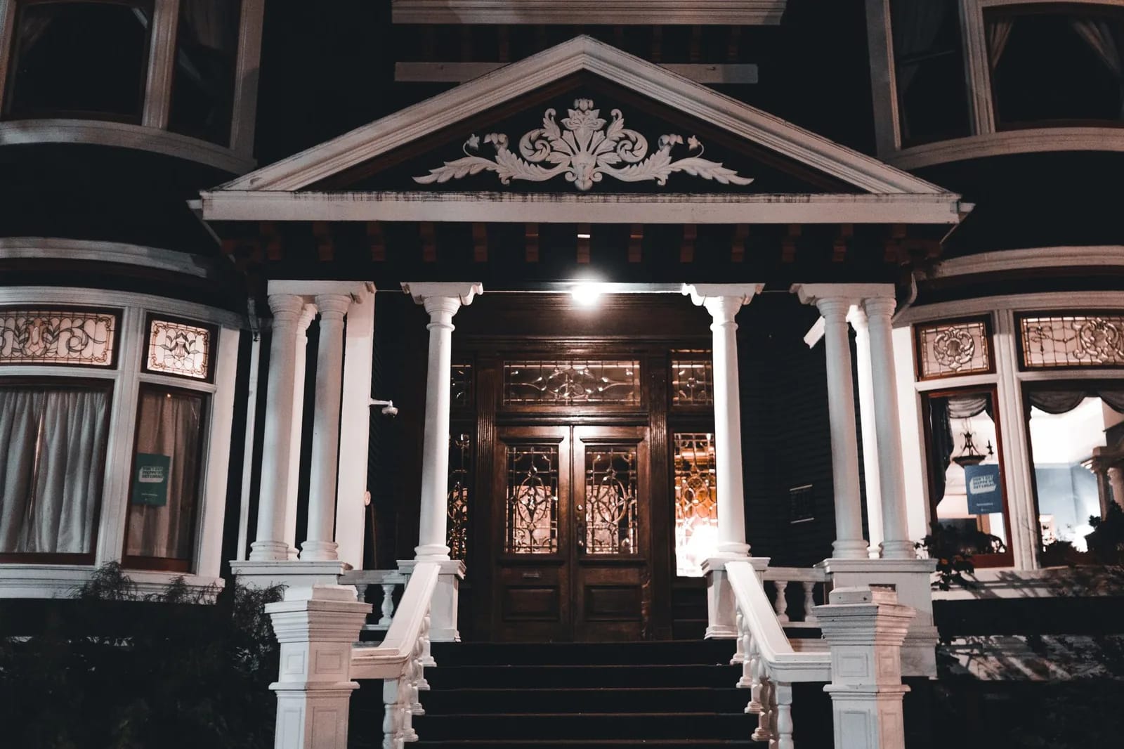 The illuminated front entrance of a Victorian house with ornate woodwork and a pedimented porch at night