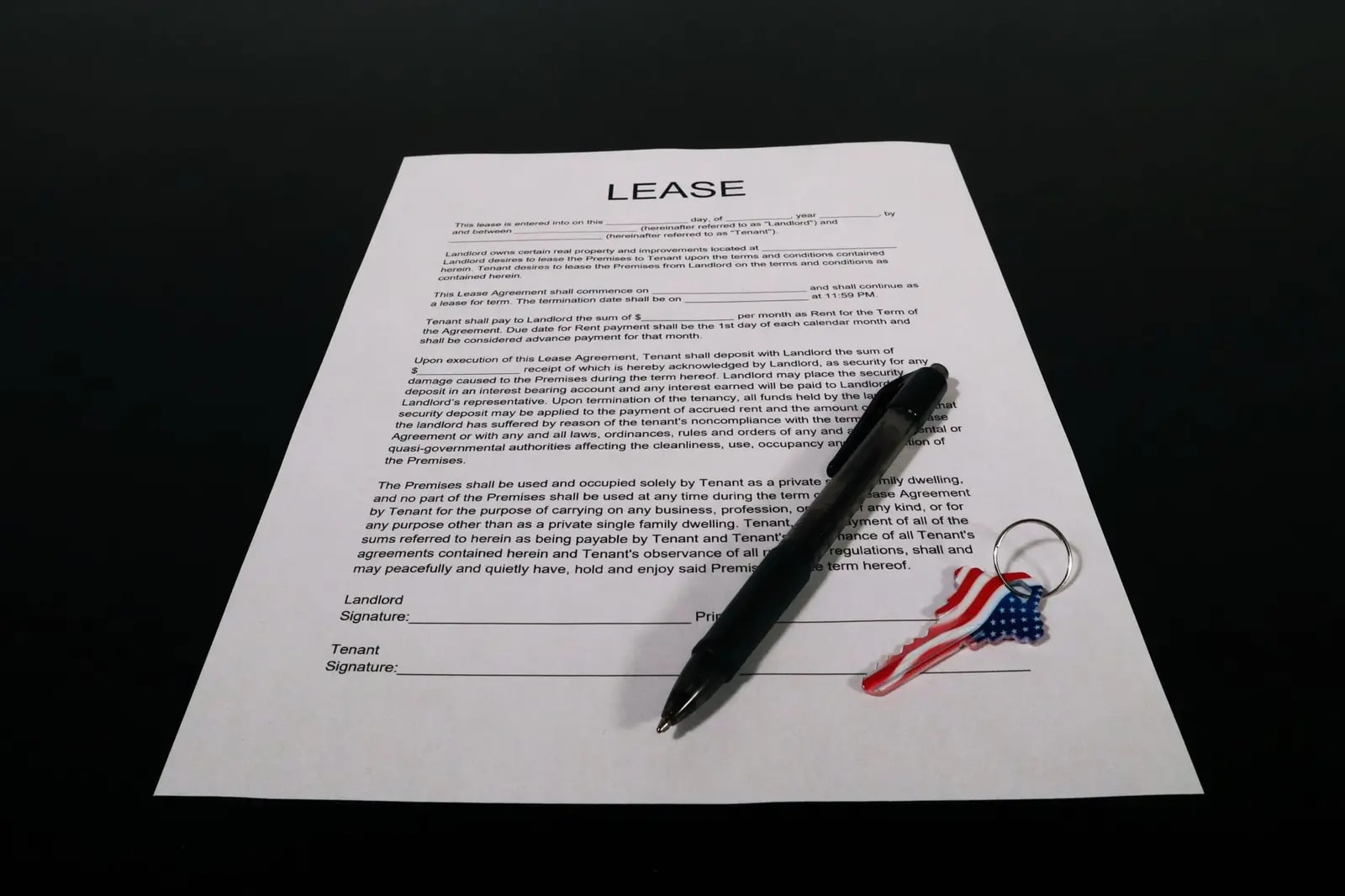 A printed lease agreement with landlord and tenant signature lines, a pen and a small flag keychain