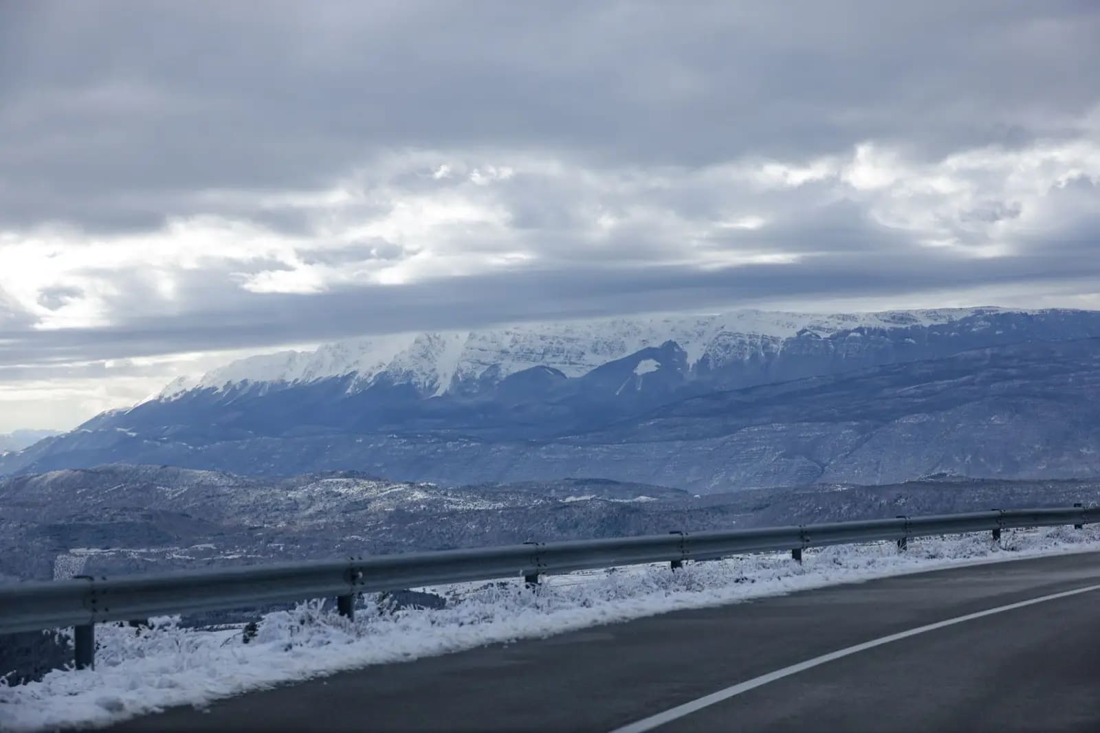 A winding road with snowy mountains under a cloudy sky creates a picturesque winter scene