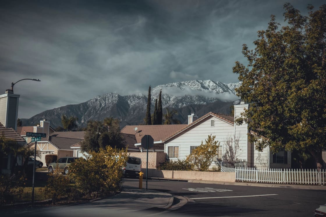 A suburban street of houses with a white fence and a snow-covered mountain behind