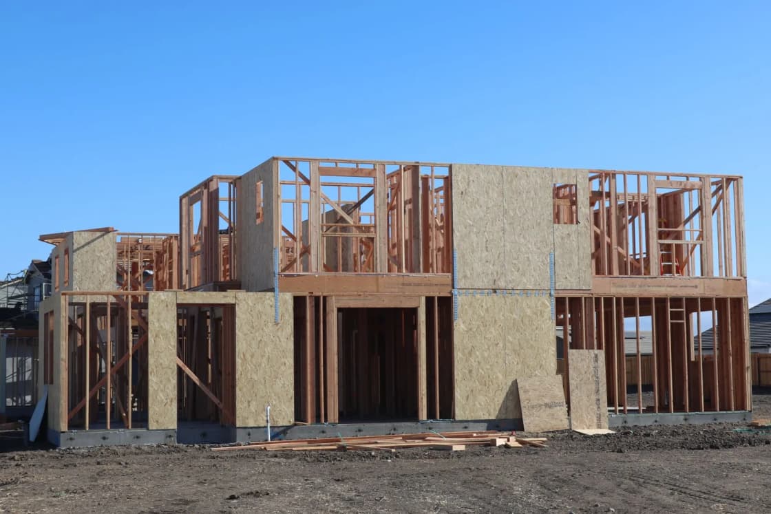 The wood frame of a new two-story house under construction, with sheathing on its walls and a dirt lot in front.