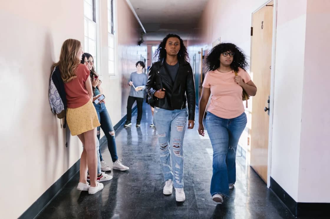 Students walking and talking in a bright school hallway lined with windows