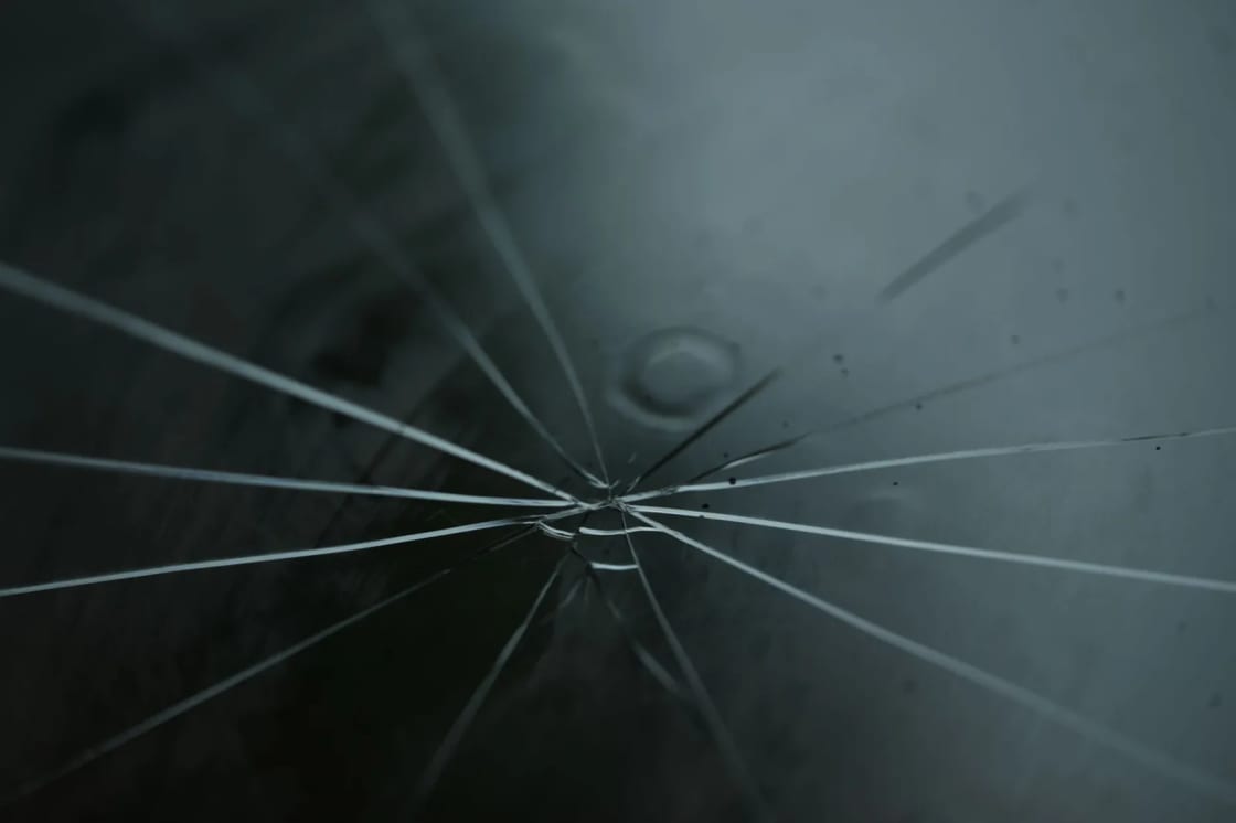 A radial crack spreading outward in fine lines across a pane of dark glass