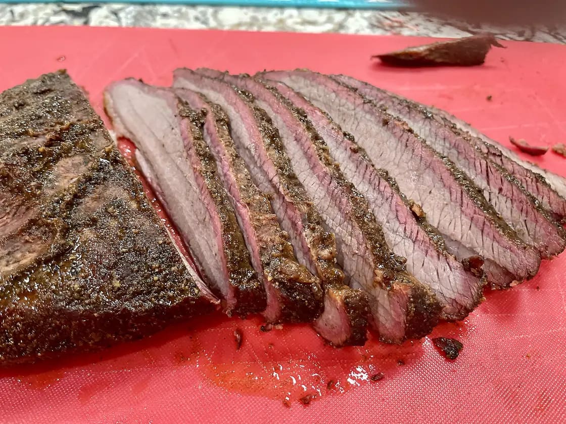 Slices of smoked beef brisket with a dark peppered bark and a pink smoke ring, fanned out on a red cutting board