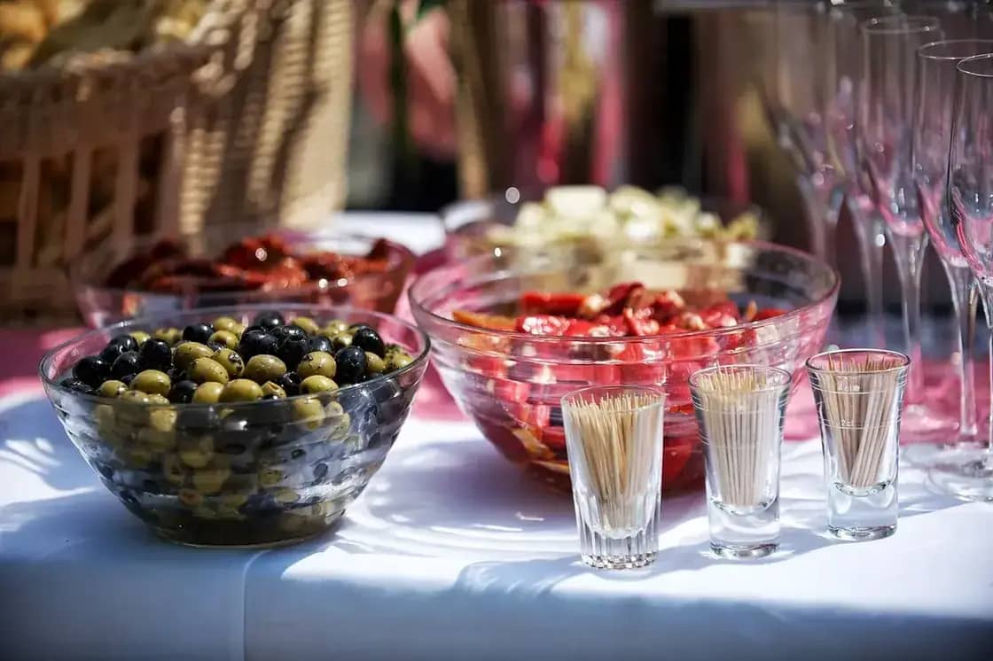 A catered buffet table set with bowls of olives, salad and rows of glassware