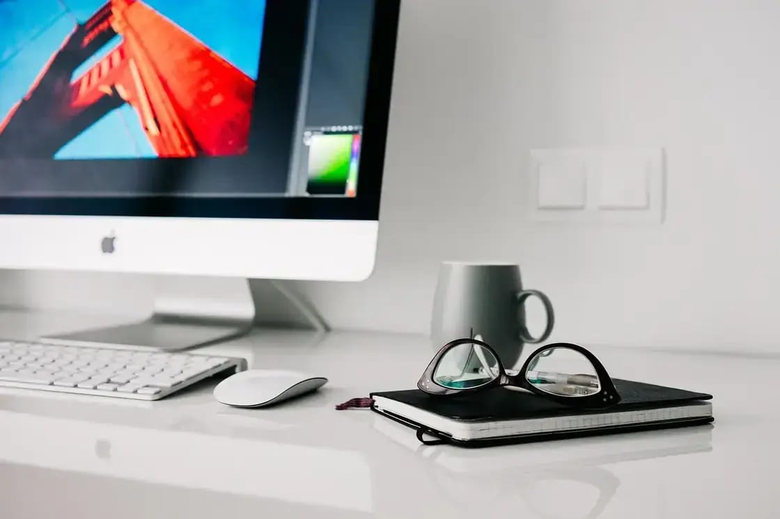 A desktop computer, keyboard and notebook on a white desk