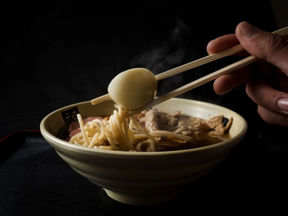Chopsticks lifting a soft-boiled egg from a bowl of ramen