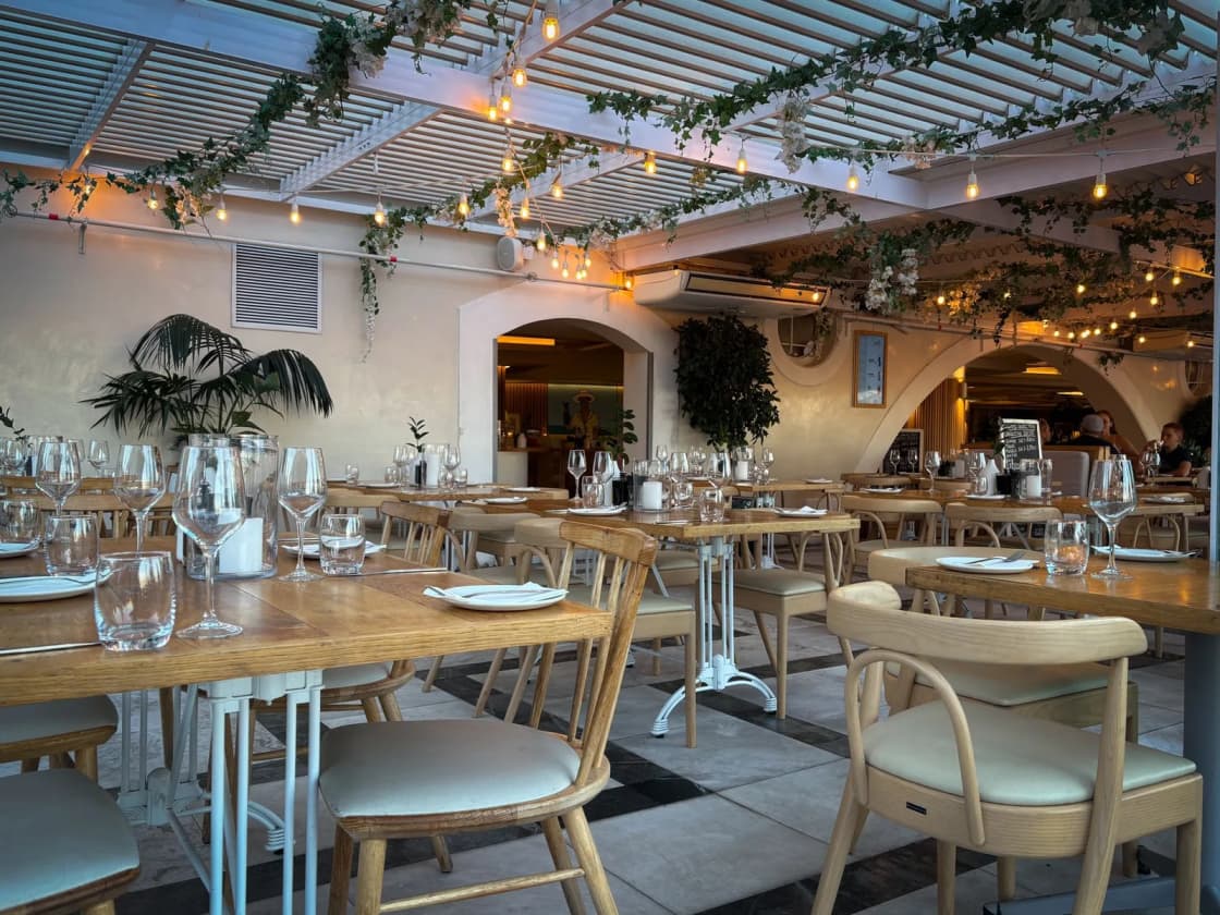 A dining room of set tables under warm lights and hanging greenery