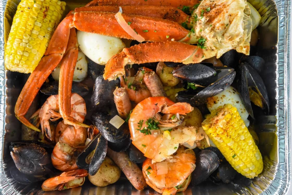 A seafood boil of snow crab legs, mussels, shrimp, corn and potatoes in a foil tray