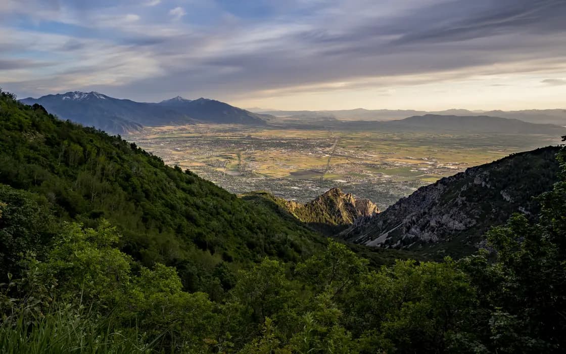 The south end of Utah Valley seen from Kyhv Peak Road, formerly Squaw Peak Road, in the mountains east of Provo, with forested slopes falling away in the foreground and the Wasatch ridgeline receding into haze