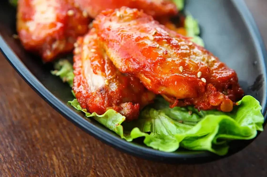 Chicken wings in red sauce served over lettuce in a dark bowl