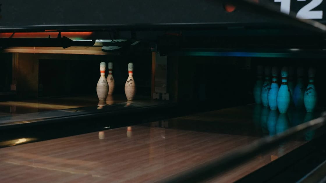 Bowling pins standing at the end of a polished lane in a dimly lit alley
