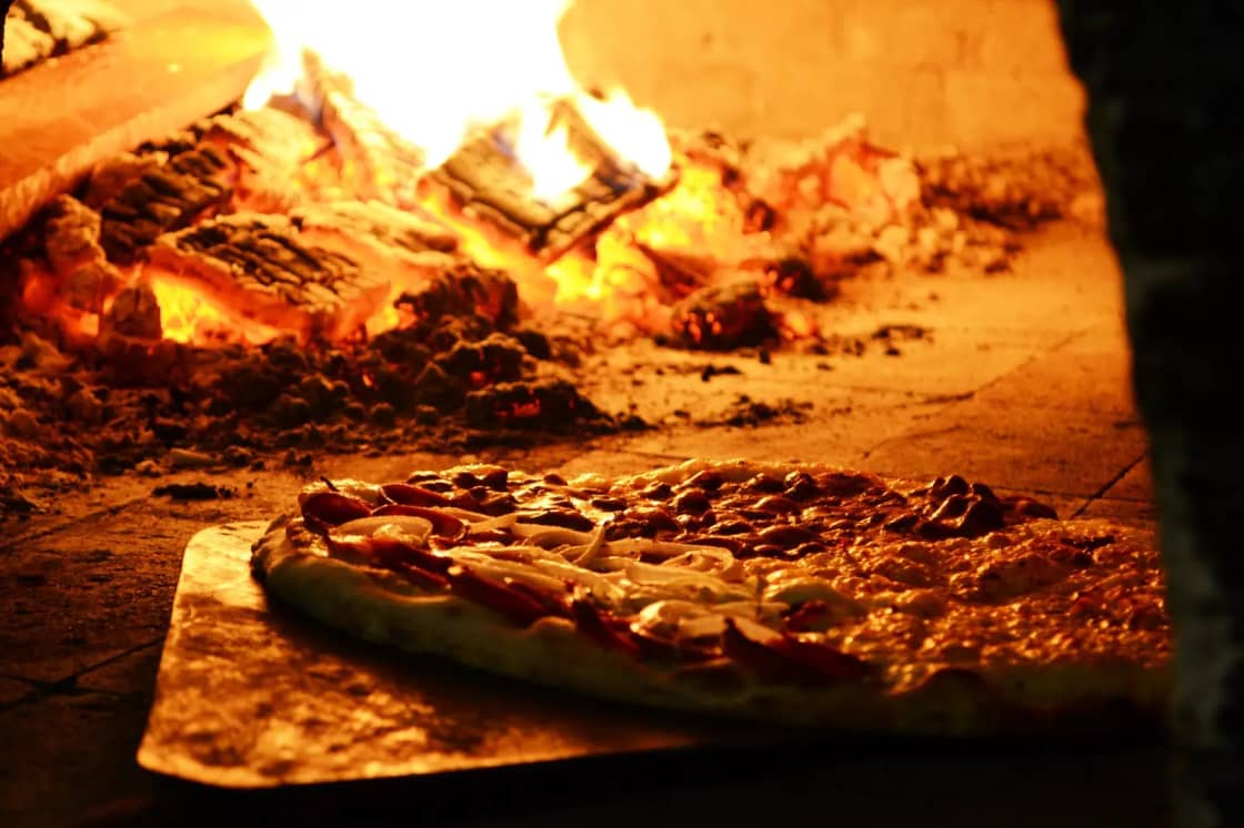 A pizza cooking in a traditional wood-fired brick oven