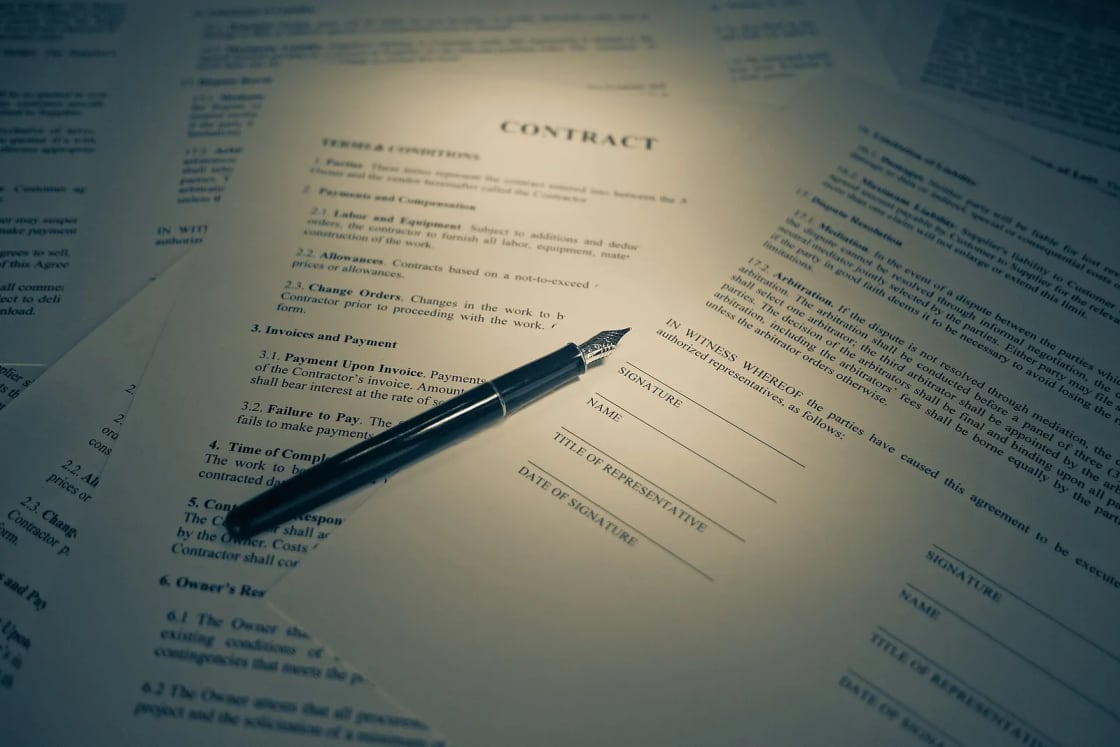 A fountain pen resting on a printed contract with blank signature and date lines.