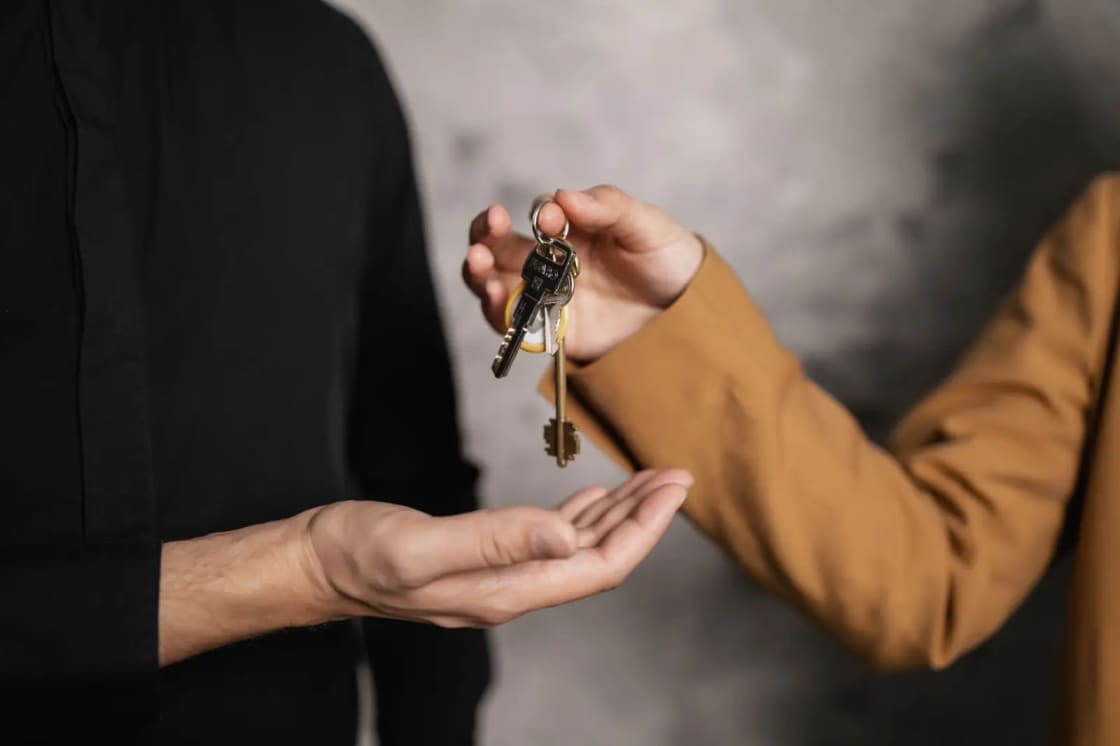 Two pairs of hands passing a set of keys between them against a plain dark background
