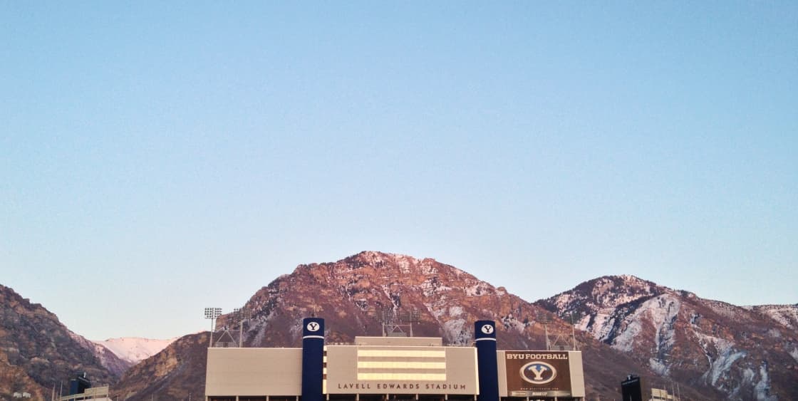 The roofline and twin blue towers of LaVell Edwards Stadium below snow-streaked Wasatch peaks at first light, the stadium name lettered across the front