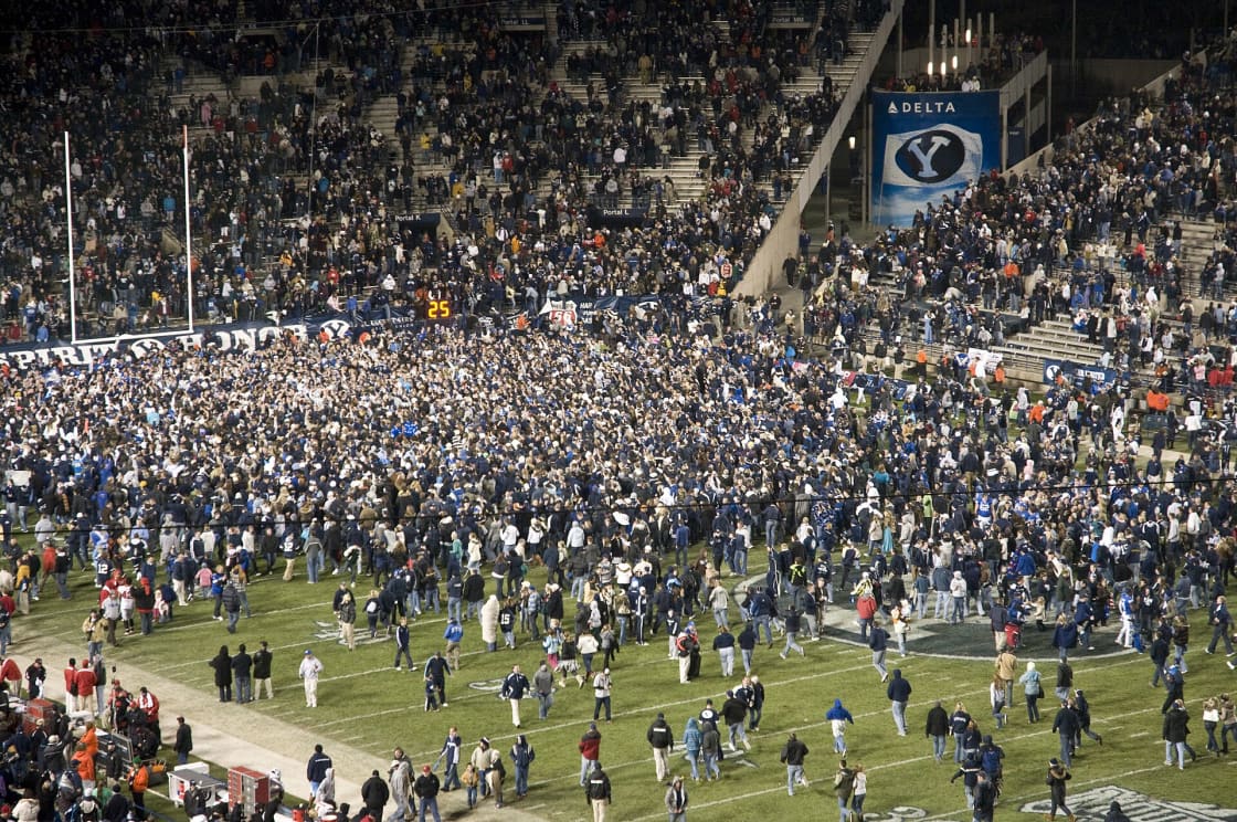 Thousands of fans crowding onto the field at LaVell Edwards Stadium after a night game, with the stands behind them still full