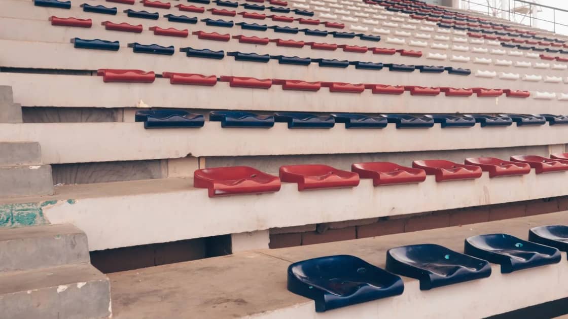 Rows of empty red and blue plastic seats in an outdoor stadium