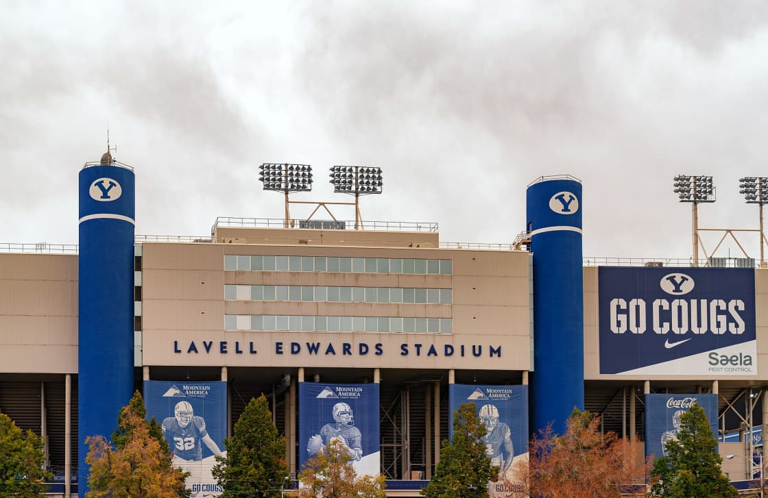 The exterior facade of LaVell Edwards Stadium in Provo, its name in blue letters below two tall blue towers marked with the BYU Y, autumn trees along the front