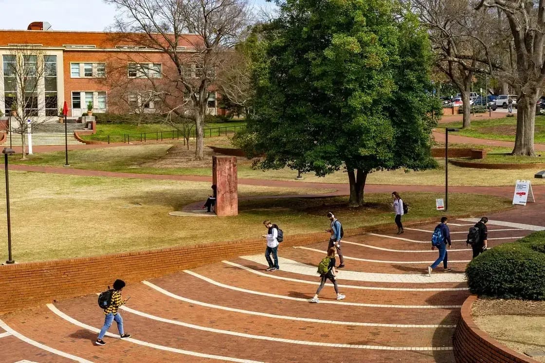Students crossing a brick campus plaza between academic buildings