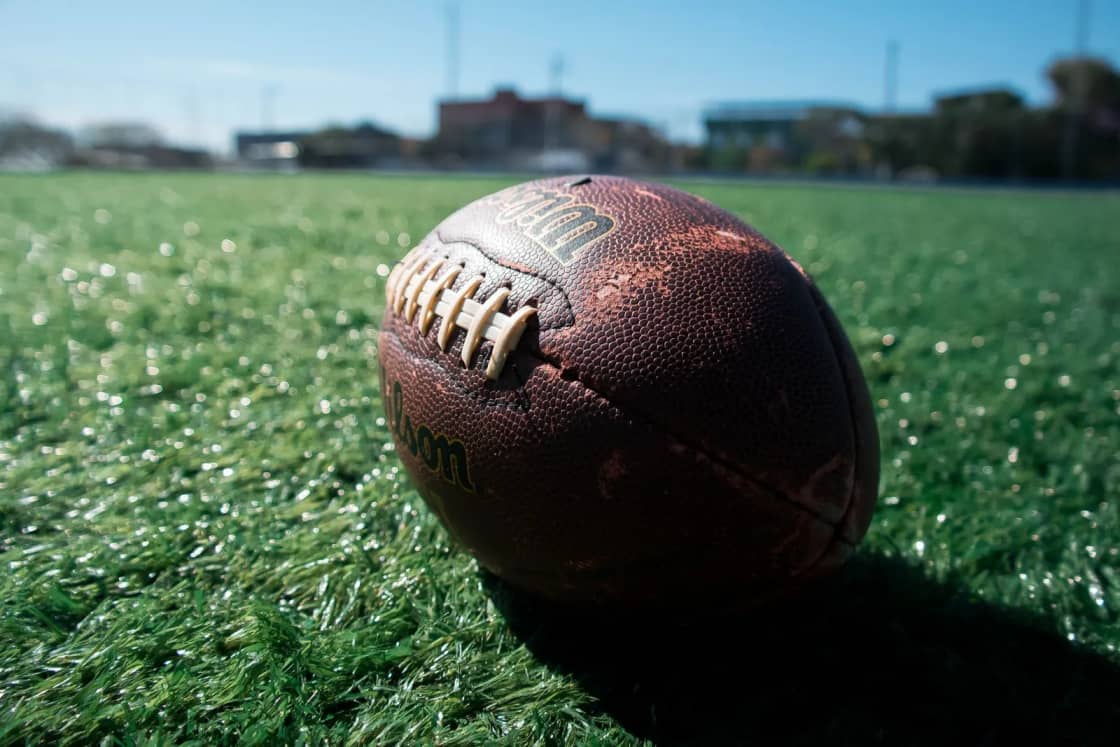 A worn leather football resting on bright green turf on a sunny day