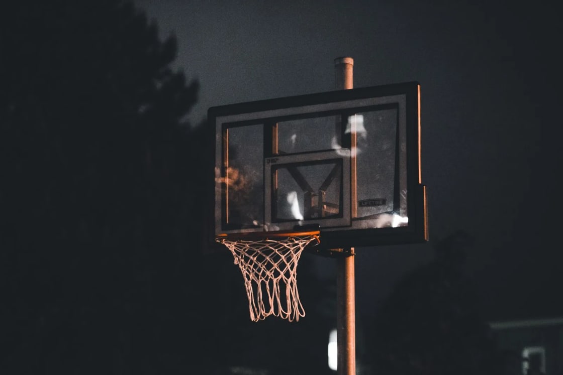 An outdoor basketball hoop and backboard lit against a dark night sky