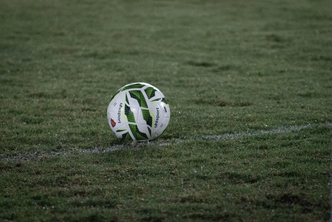 A white and green soccer ball on a painted line of a grass field at dusk