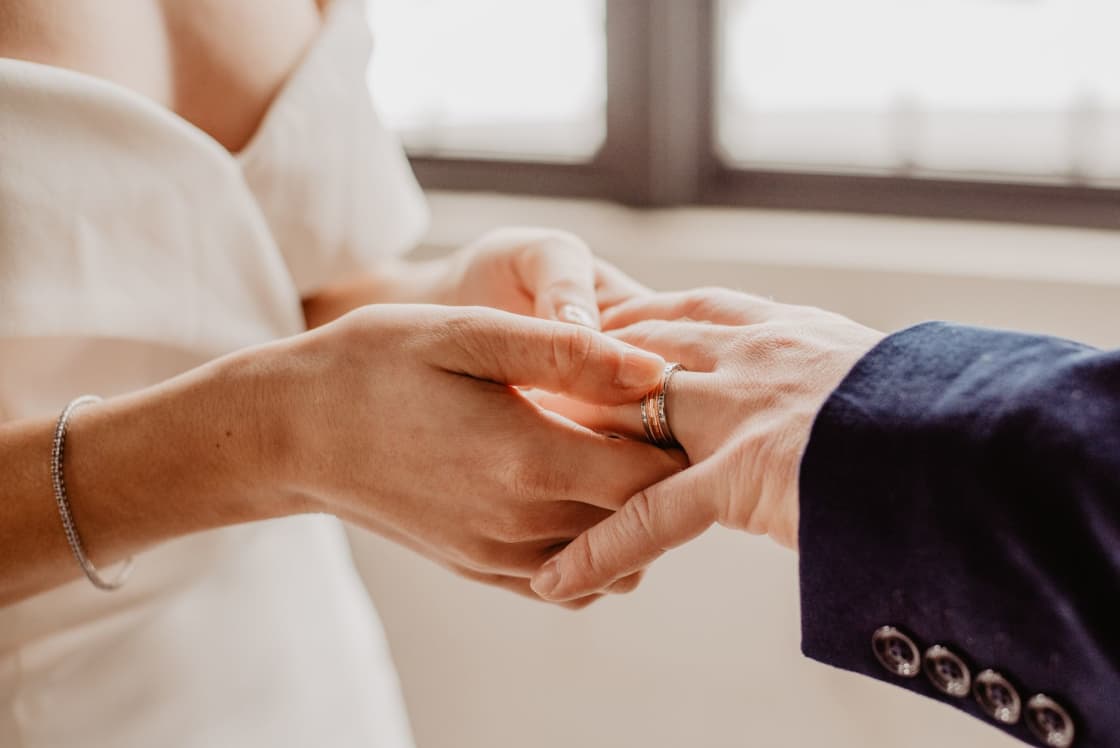 Two people's clasped hands during a wedding ceremony, one hand wearing a wedding ring