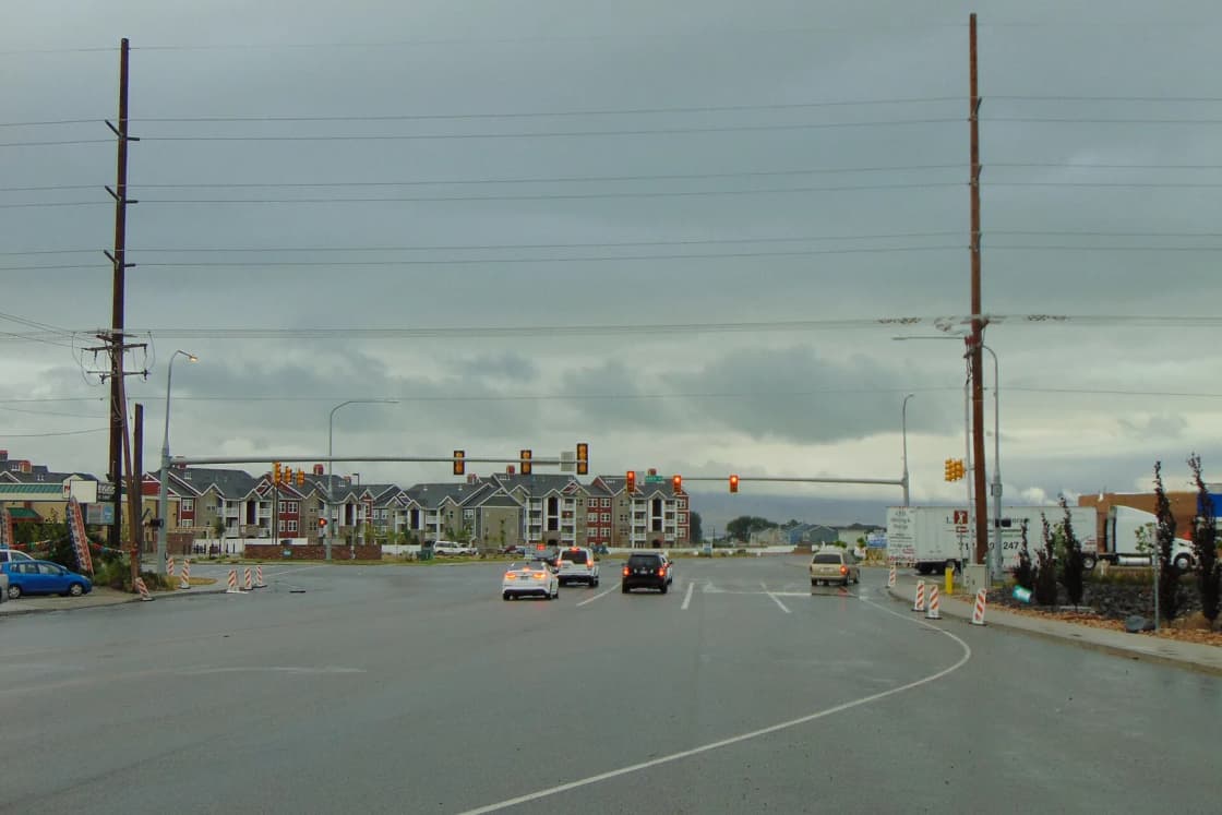 Apartment buildings beside a wide intersection on Mill Road in Vineyard, Utah, under a cloudy sky.