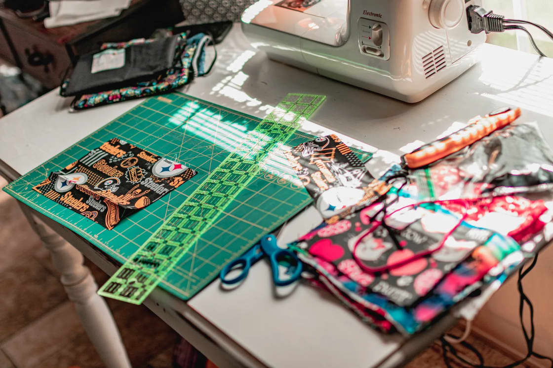 Patterned fabric pieces, scissors and a quilting ruler on a green cutting mat beside a sewing machine.