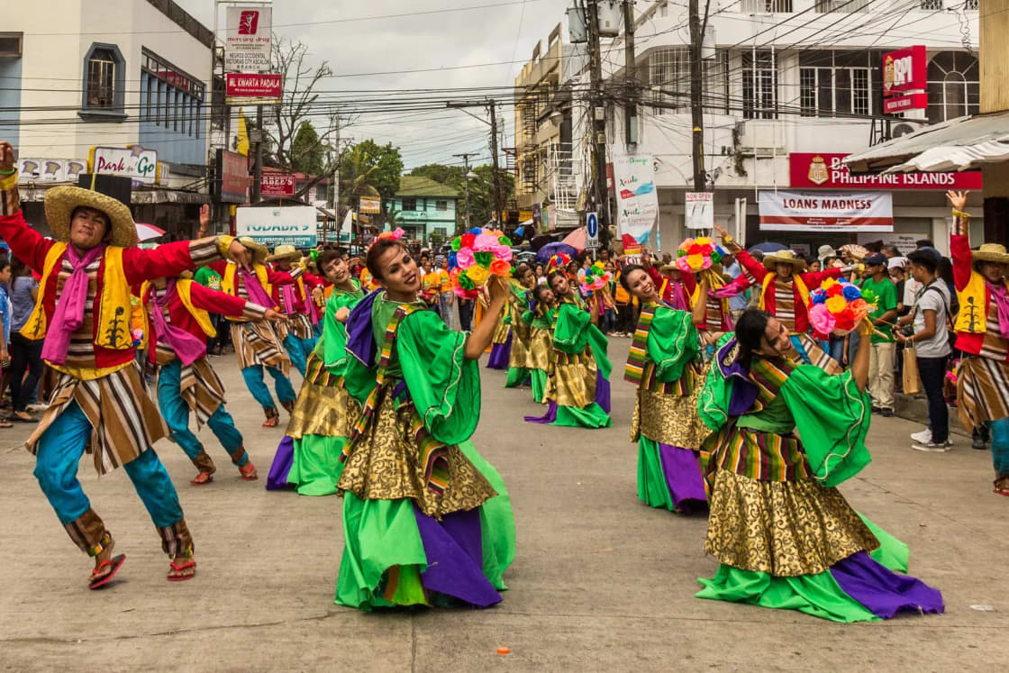 Folk dancers in bright green and pink costumes perform in a street parade lined with spectators.