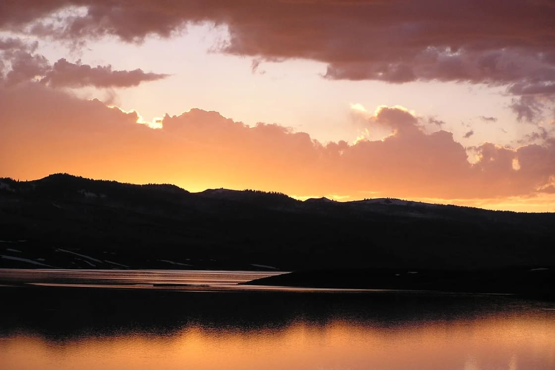 Sunset glowing orange over Strawberry Reservoir and the dark, snow-patched hills around it.