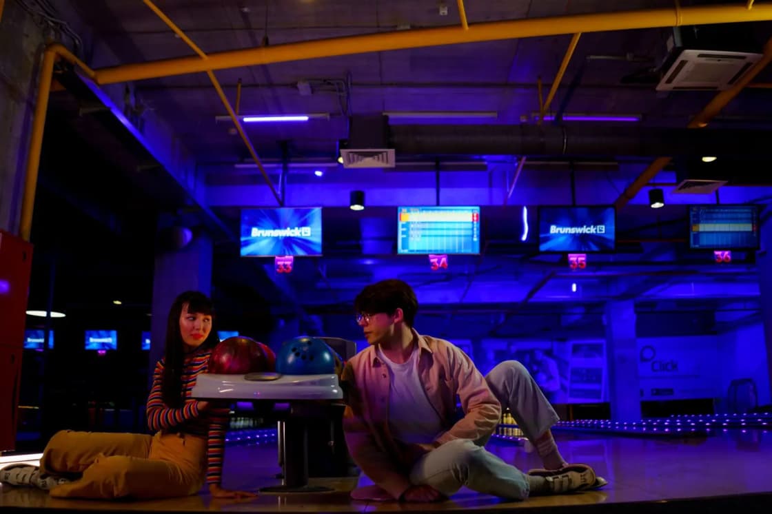 A stylish young couple hanging out in a neon-lit bowling alley enjoying a casual game