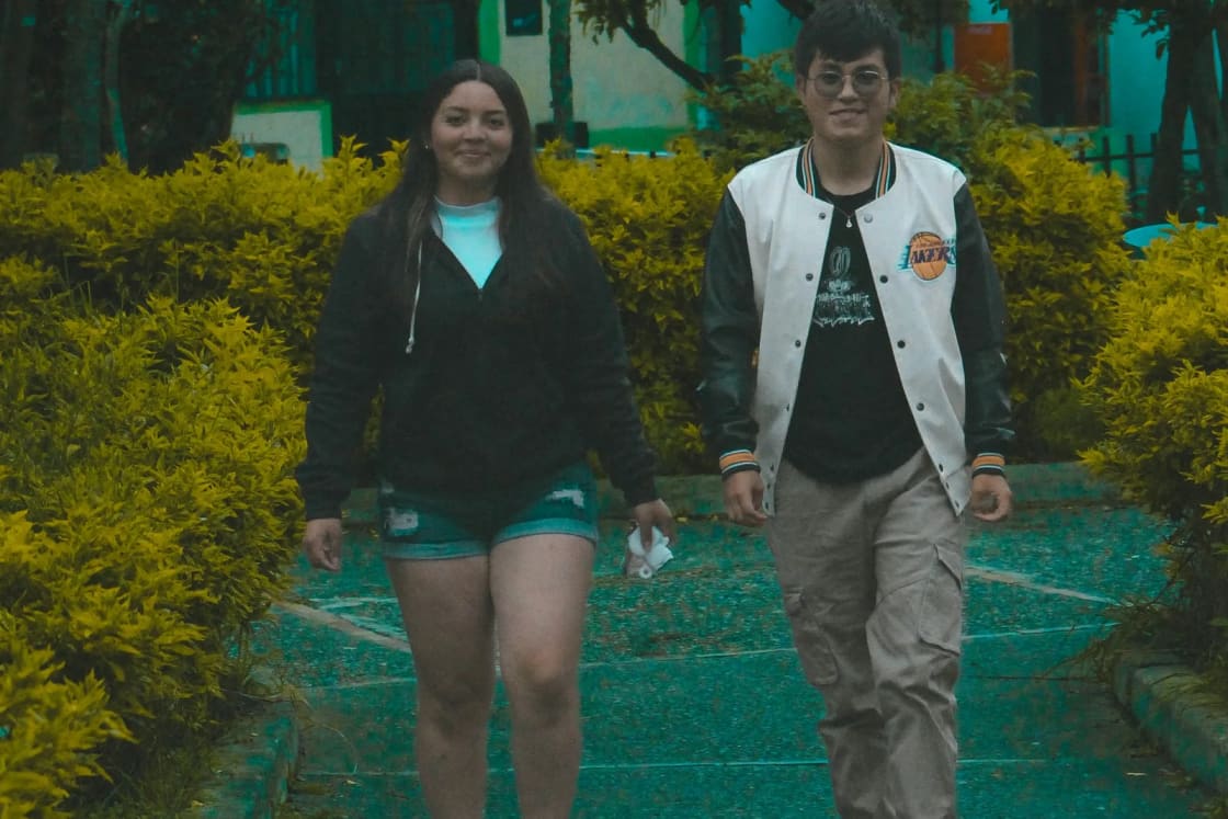 A young man and woman walking side by side down a garden path between trimmed yellow-green hedges