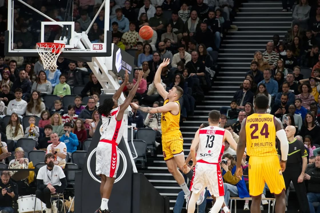 Players in white and yellow jerseys contest a rebound under the basket in front of a full arena crowd — game night at the Delta Center from Utah Valley