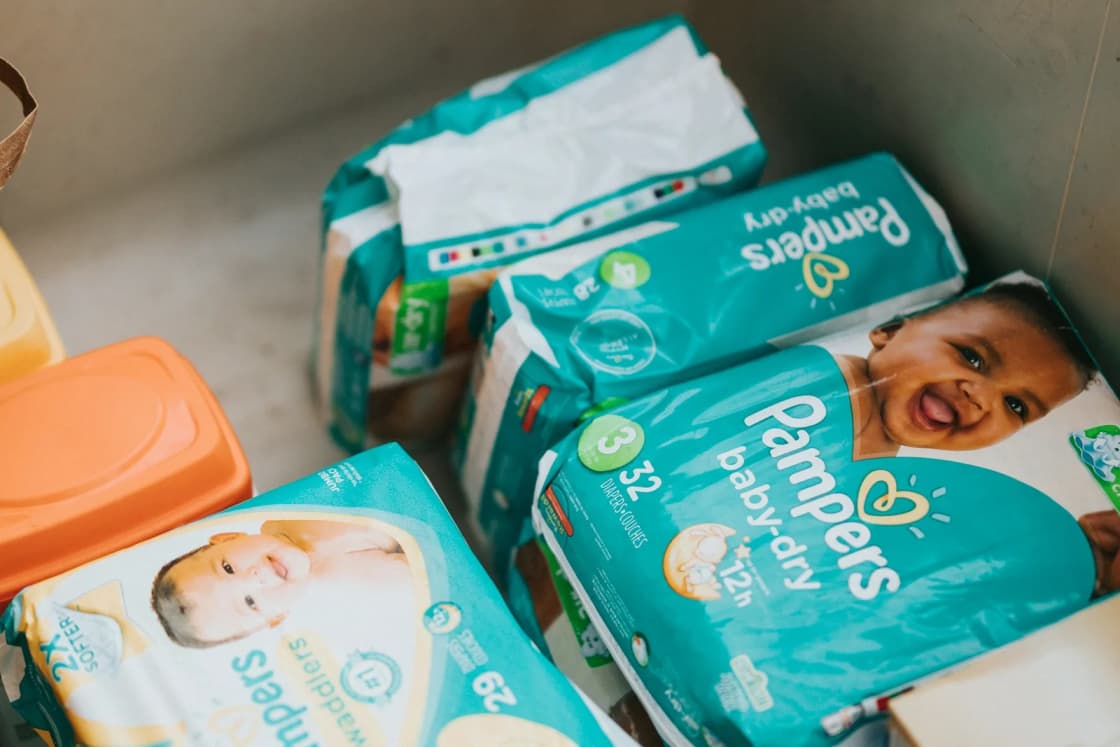 Packages of disposable diapers in several sizes stacked in an open cardboard box, the kind of supply pantries hand out.