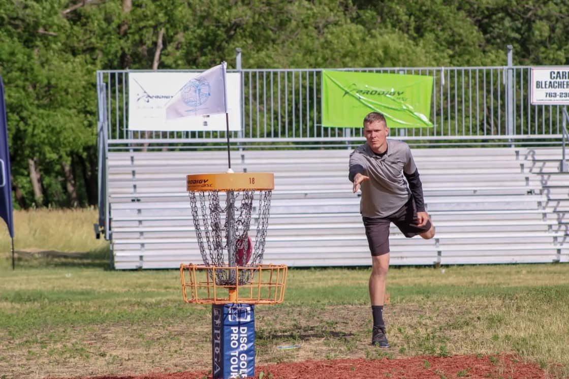 A player throwing a disc toward a chain disc golf basket